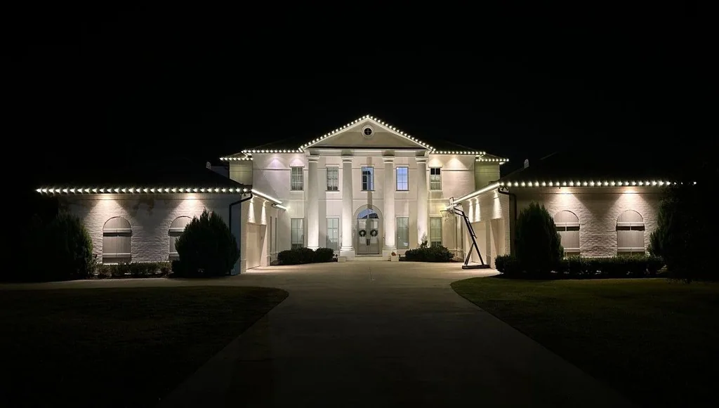 Grand symmetrical estate at night outlined in warm-white lights with a lit columned entrance