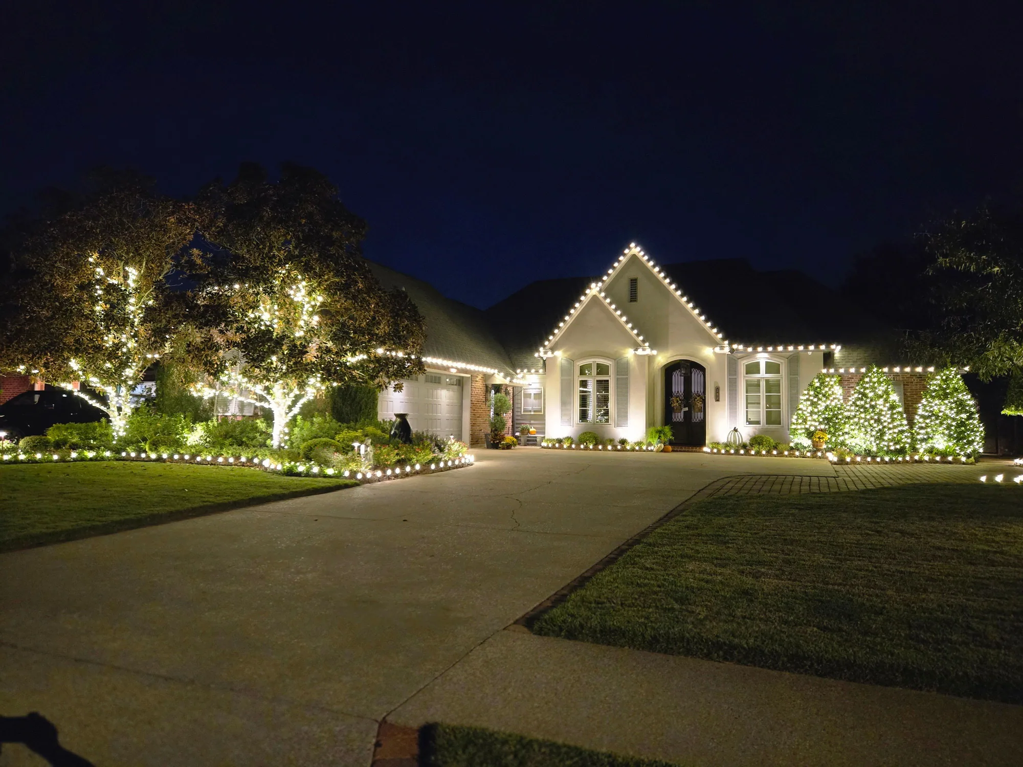 Acadian-style home at night with warm-white roofline lighting and softly lit trees in the yard