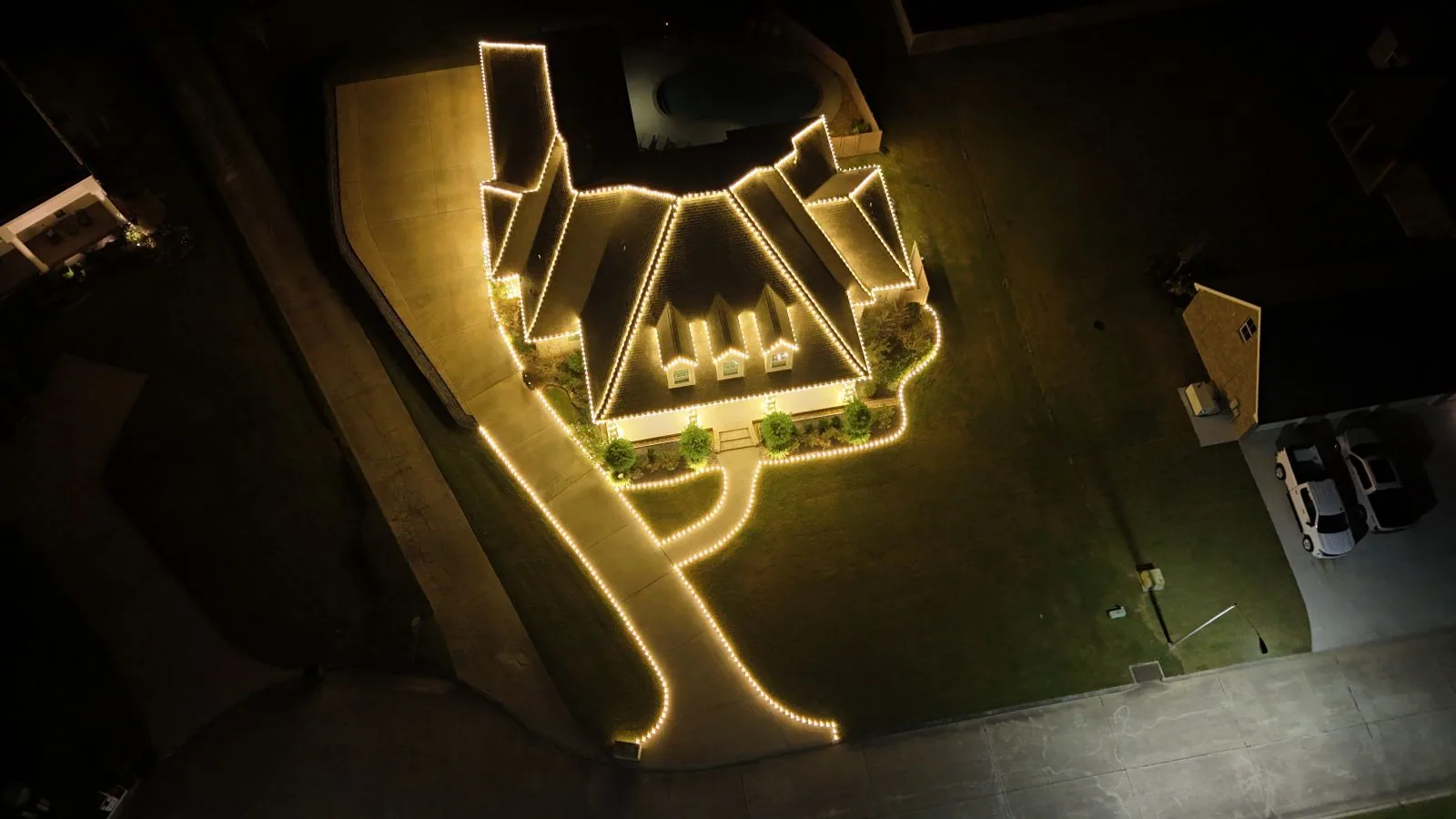 Aerial night view of a property with its rooflines and driveway outlined in warm-white lights
