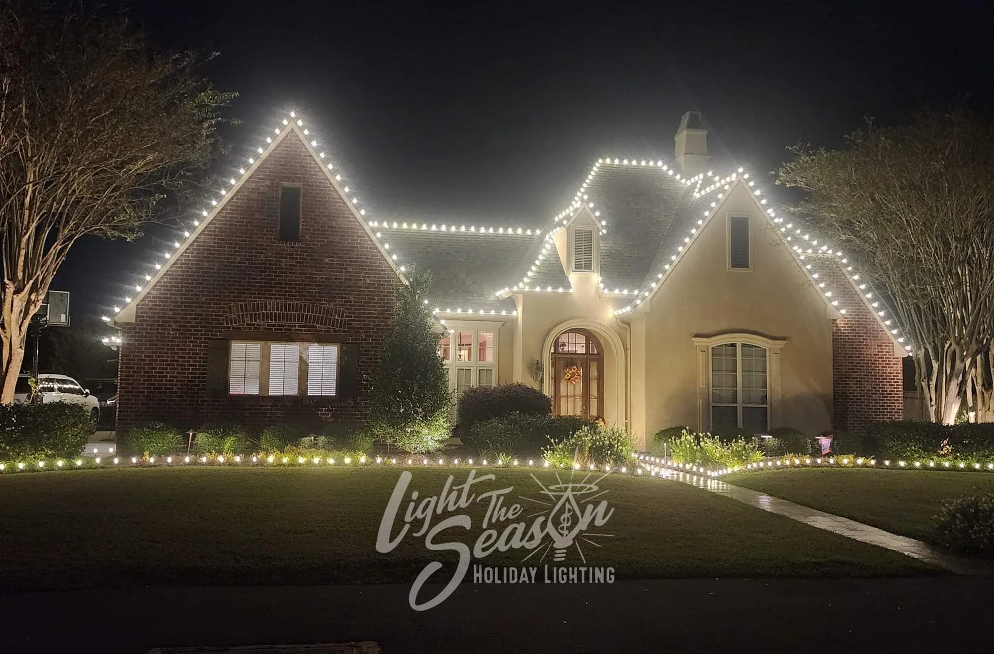 Brick home at night with warm-white roofline lights and landscape beds outlined in lighting