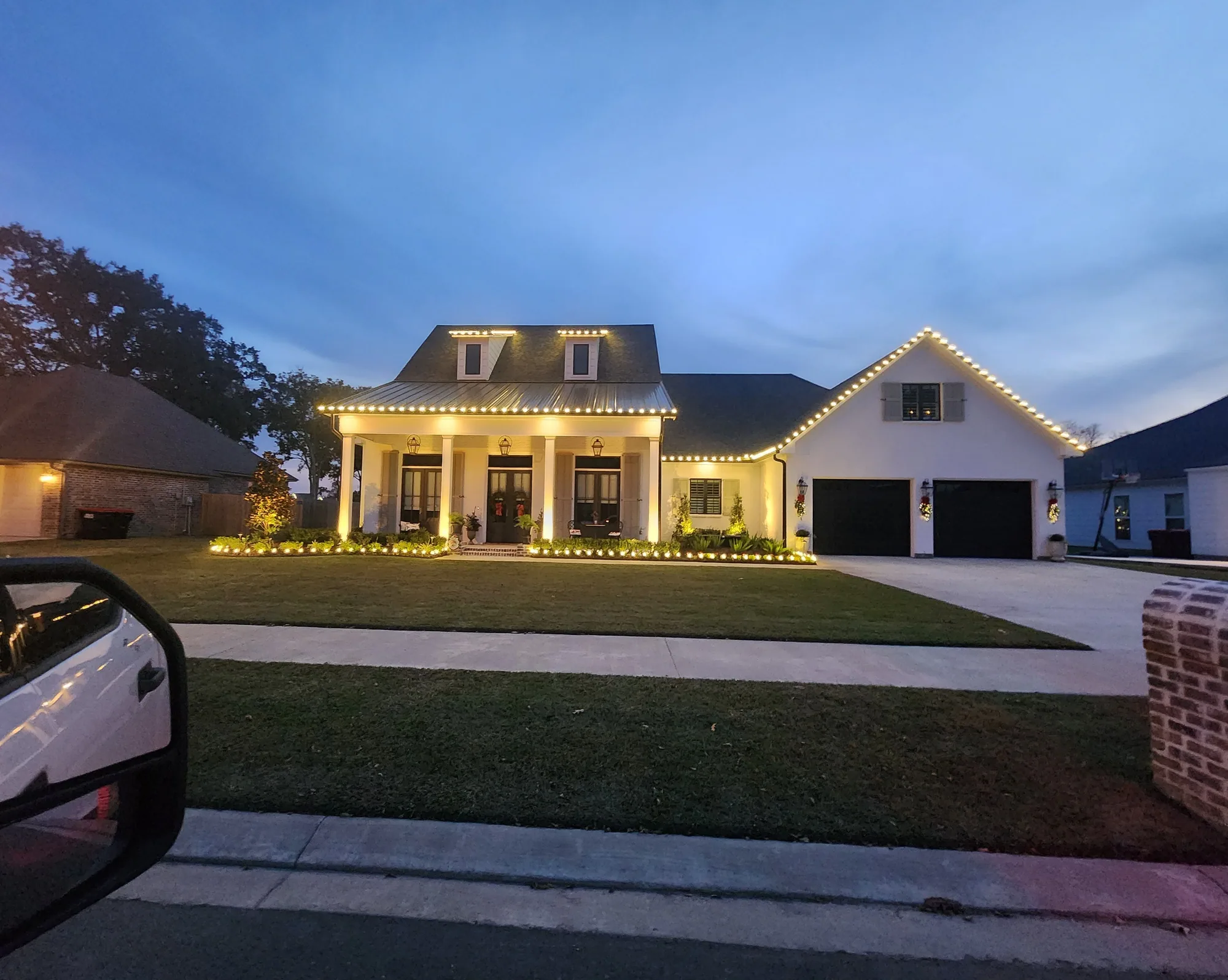 Acadian home at twilight with warm-white roofline lights and a lit front porch