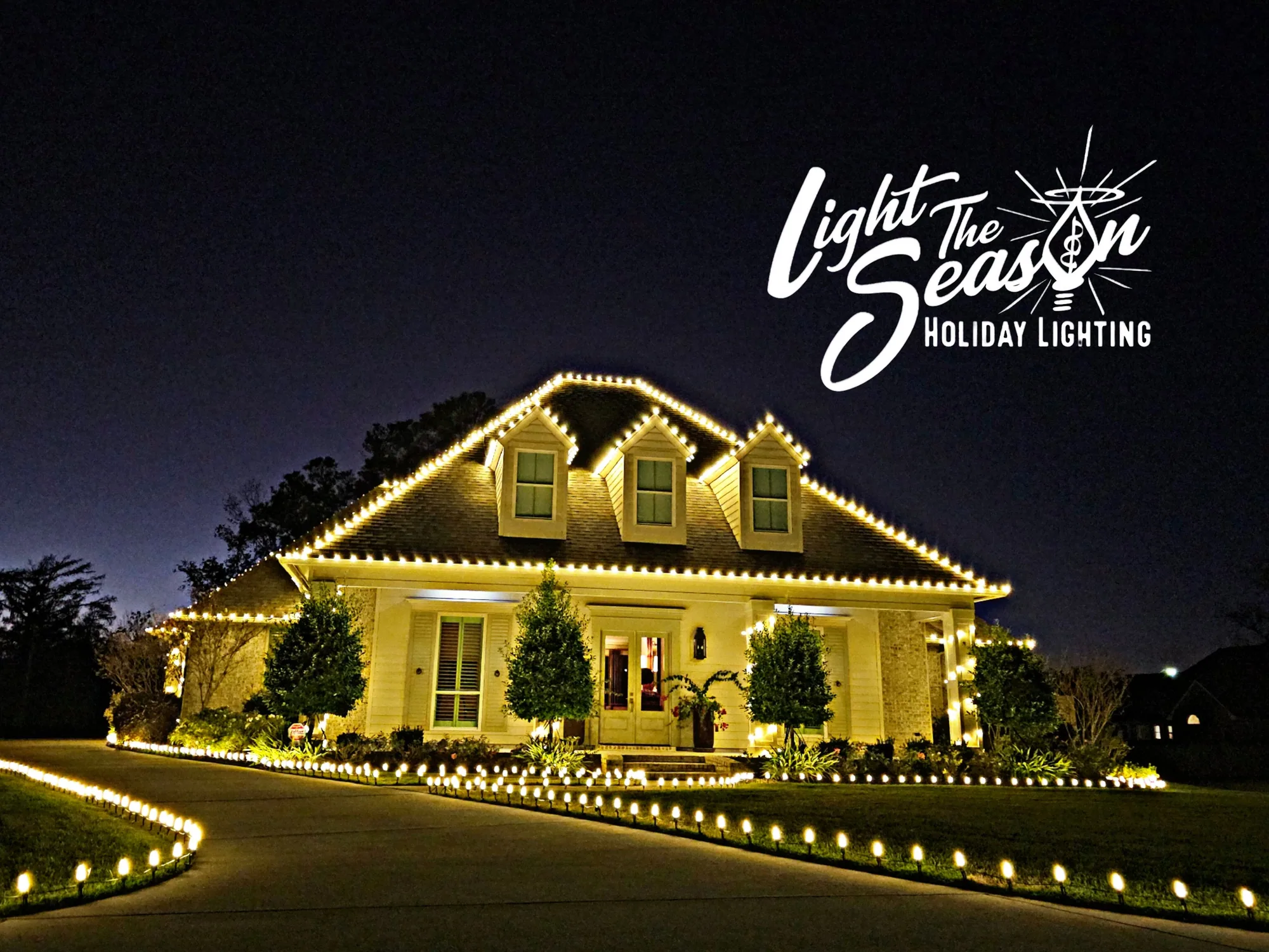 Brick Acadian home at night with warm-white roofline lights and warm landscape uplighting