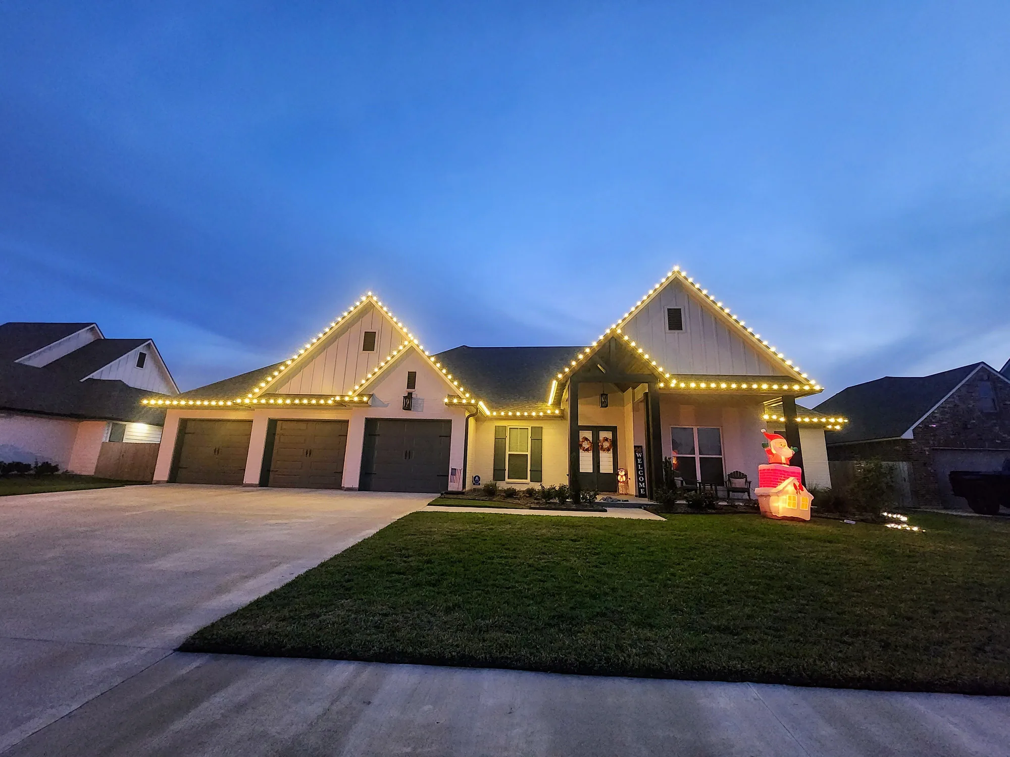 Modern farmhouse with a three-car garage at twilight, roofline outlined in warm-white lights