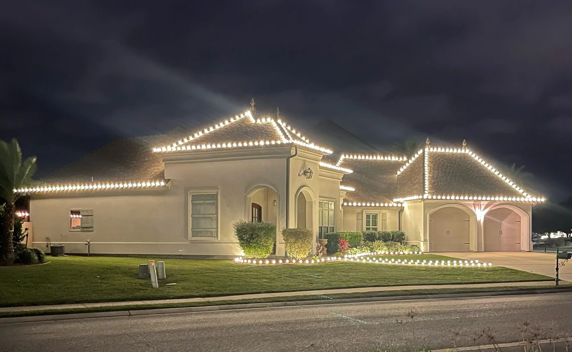 Stucco home at night with warm-white roofline lighting and landscape lighting along the front