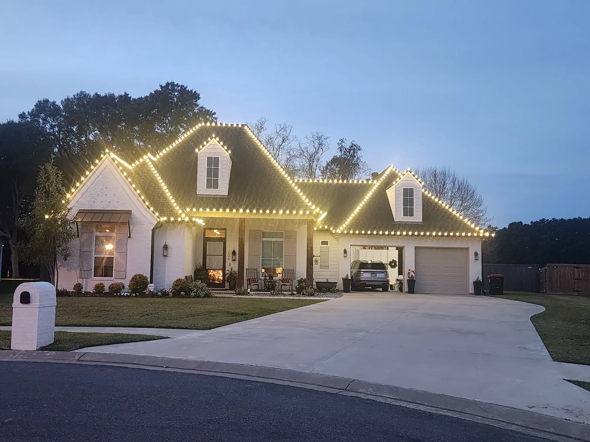 White home at dusk with warm-white Christmas lights along the roofline